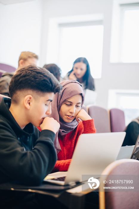 Friends discussing over laptop during lectures in university