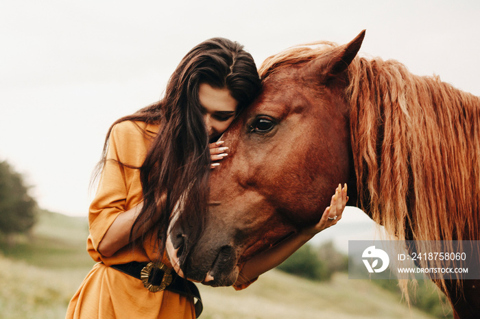 Portrait of a amazing woman with dark long hair embracing her best friend , a brown horse .