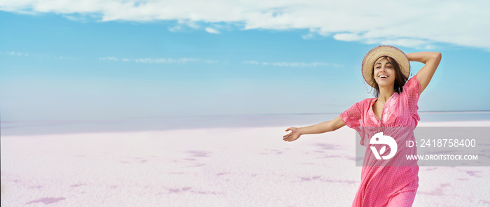 蓝天白色盐滩土地上，身穿粉色连衣裙，戴着张开双臂的帽子的全景图像自由女性