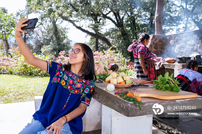 Chica haciendose una selfie con el telefono celular. Familia cocinando en una estufa de leña al aire