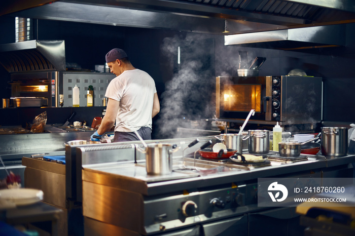 cook stands with his back, Cooking in a modern kitchen, in a restaurant. low key. Copy space for tex