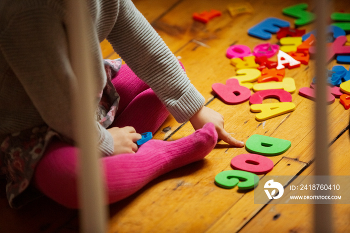 Low section of girl arranging colorful alphabets on hardwood floor at home