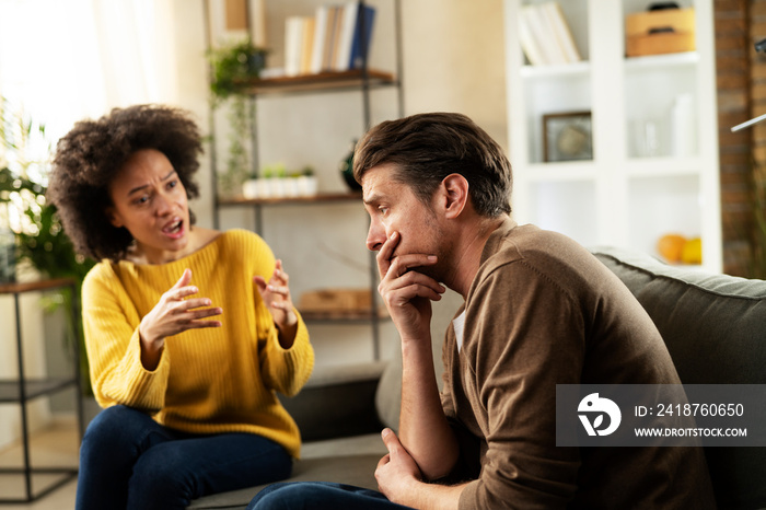 Frustrated young couple arguing at home. Stressed unhappy wife and husband sitting on cauch at home.