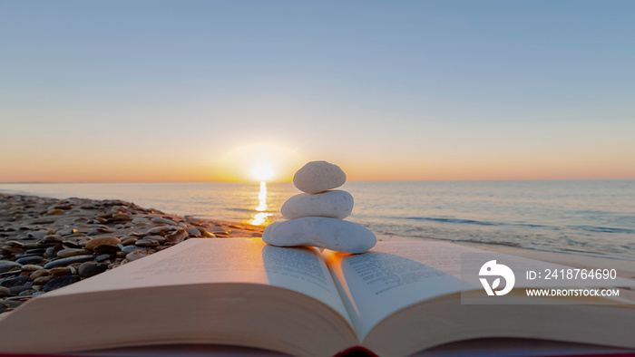 Zénitude sur la plage. Livre sur la plage avec galets blancs sur un lever de soleil.