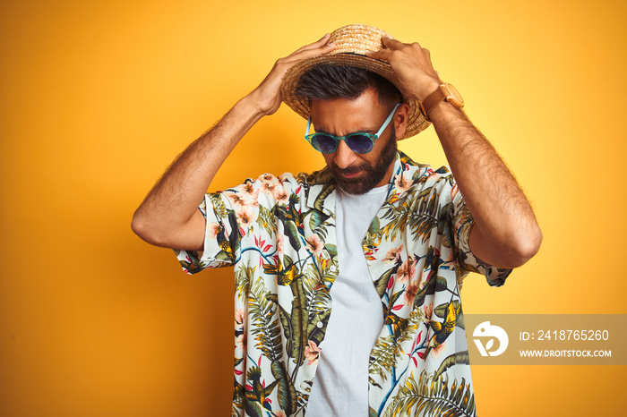 Indian man on vacation wearing floral shirt hat sunglasses over isolated yellow background suffering