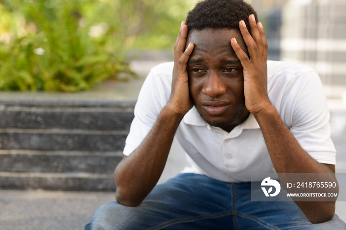 Portrait of stressed young African man looking upset while sitting outdoors