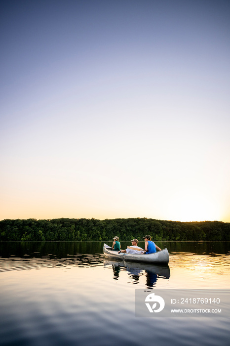 Air Force service member takes his sons canoeing at sunset out on the lake.