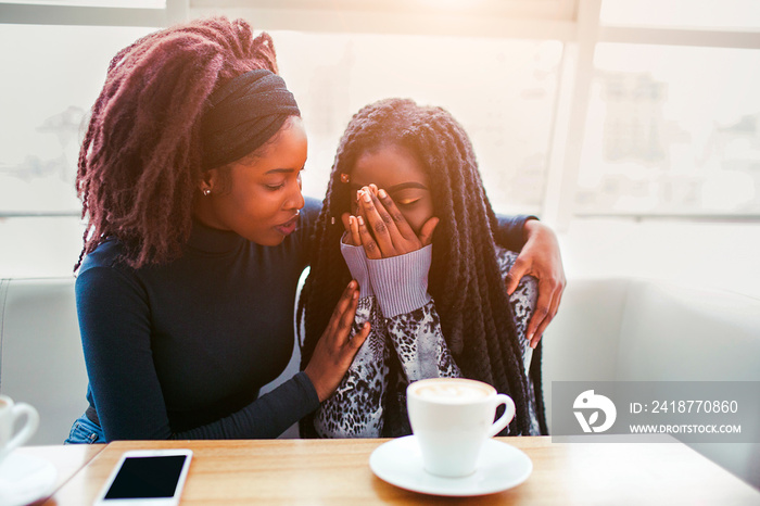 Upset youn african woman sit and cry. She covers face with hands. Her friend comfort young woman. Th