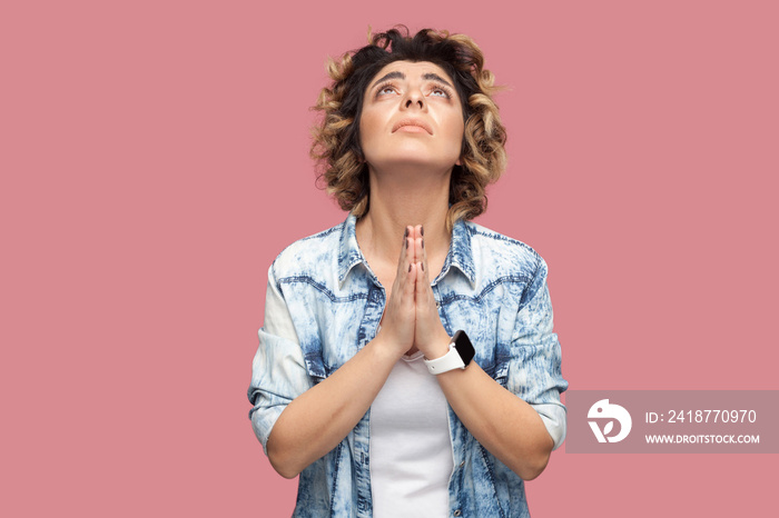 My god please help me. Portrait of hopeful young woman with curly hairstyle in casual blue shirt sta