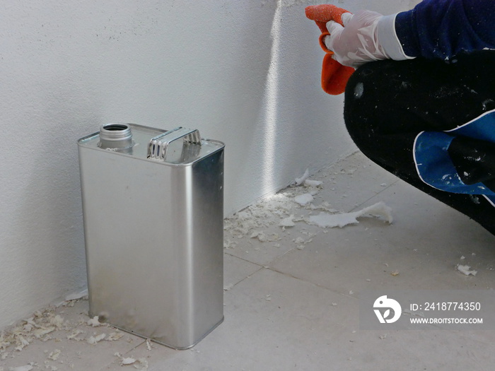 A gallon of thinner placed next to old concrete wall, while a painter is removing sticky rough glue 