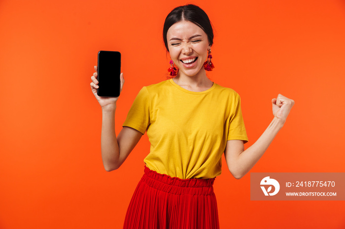 Excited happy young woman posing isolated over orange wall background showing display of mobile phon