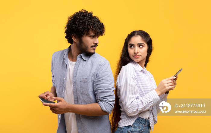 Privacy concept. Indian man trying to look at his girlfriends smartphone, woman hiding screen of he