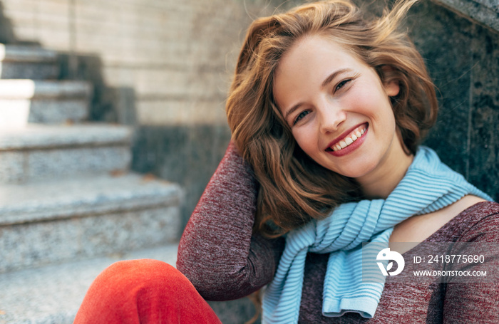 A cheerful female takes a rest outside on the street sitting on the stairs. Happy young woman studen