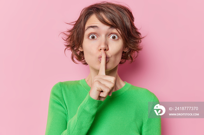 Surprised brunette woman makes silence gesture asks not to reveal her secret tells asks not to sprea