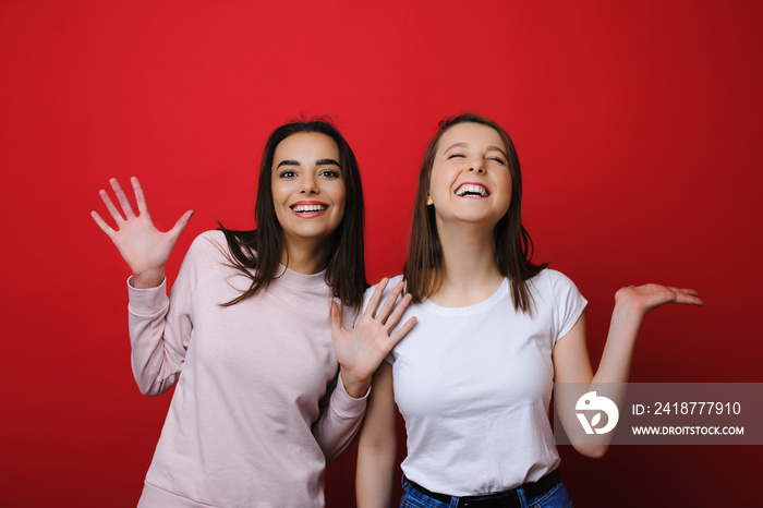 Portrait of a two amazing girls having fun laughing against a red wall in studio.