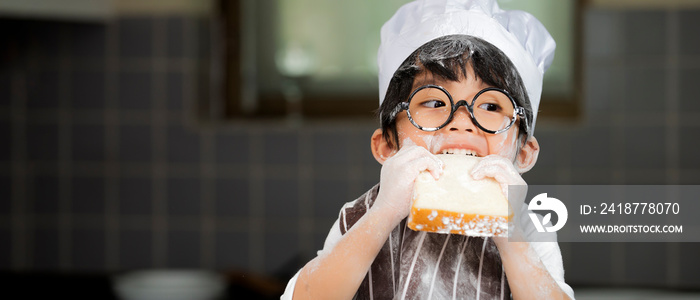 Happy cute asian  little boy in apron eating bread  in kitchen room at home