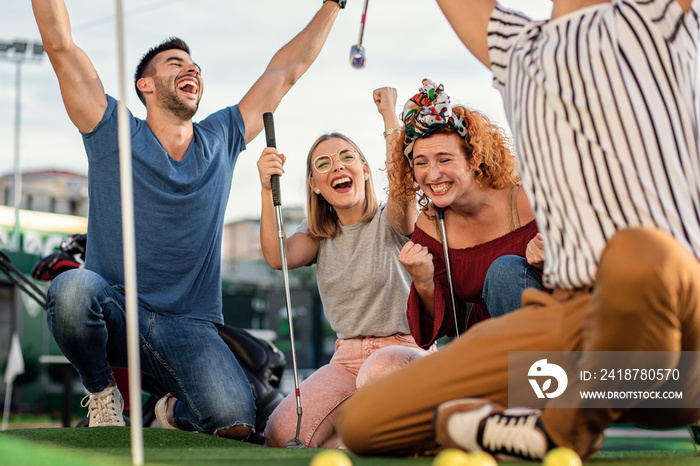 Group of smiling friends enjoying together playing mini golf in the city.