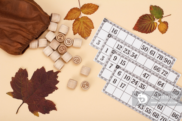 Wooden lotto barrels with brown bag and game cards on beige background.