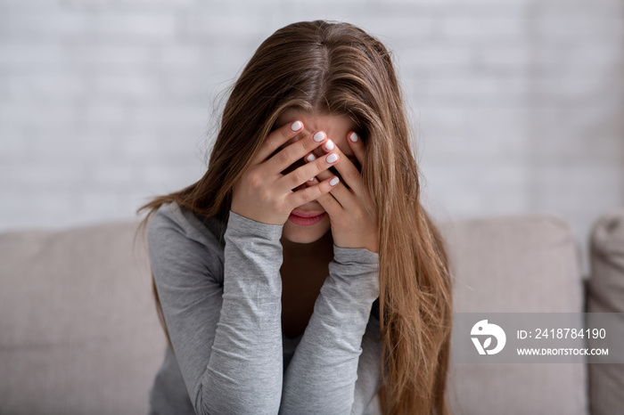 Millennial woman covering her face with hands and crying, feeling depressed or stressed