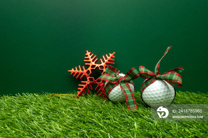 Golf ball with Christmas ribbon and snow flake are on green grass.