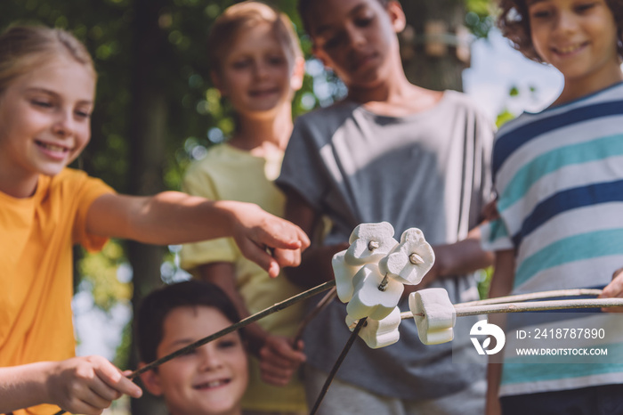 selective focus of kid pointing with finger at sweet marshmallows in sticks near multicultural boys