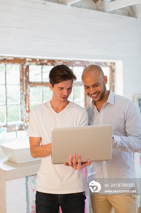 Young male roommates using laptop in kitchen