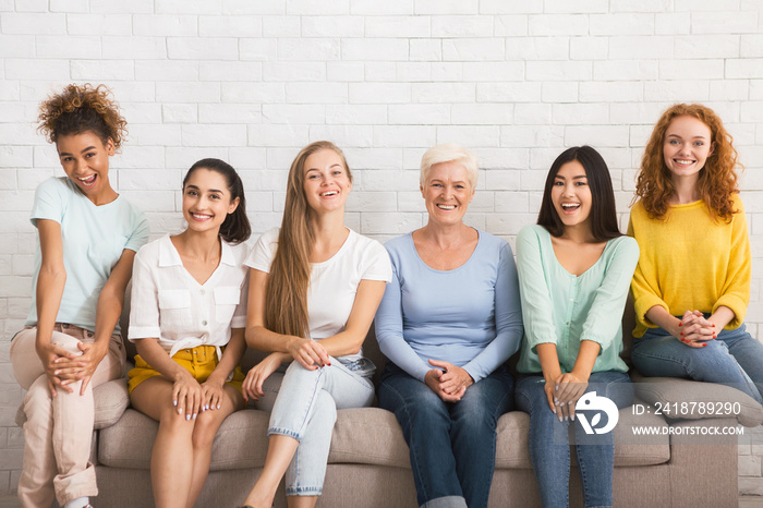 Smiling Diverse Women Sitting On Sofa Over White Brick Wall