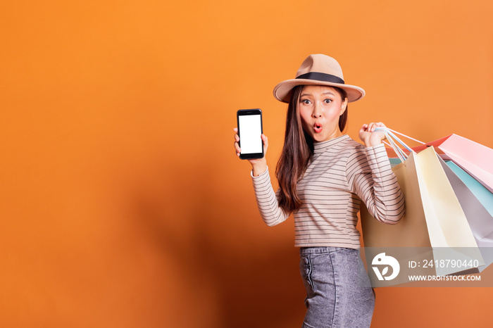 Young beautiful fashionable Asian woman holding shopping bags phone and credit card over orange back