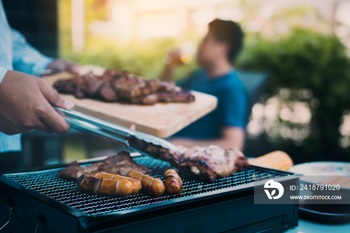 Close up asian hand man are pinching the pork on the grill and holding it to friends who are celebra