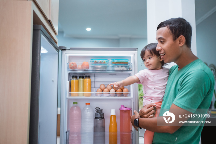 toddler asking for some food inside the refrigerator with father