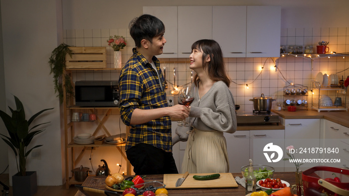 asian romantic couple flirting with each other with wine on valentine’s night date at home in the ki