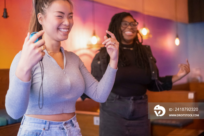 Female friends dancing while playing in video game at pub