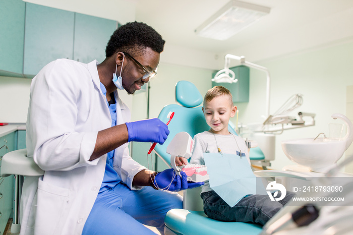 Happy smiling black dentist tells Caucasian little boy how to brush his teeth. Caries prevention, De