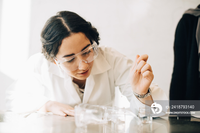 Teenage girl in lab coat learning chemistry in science class at university