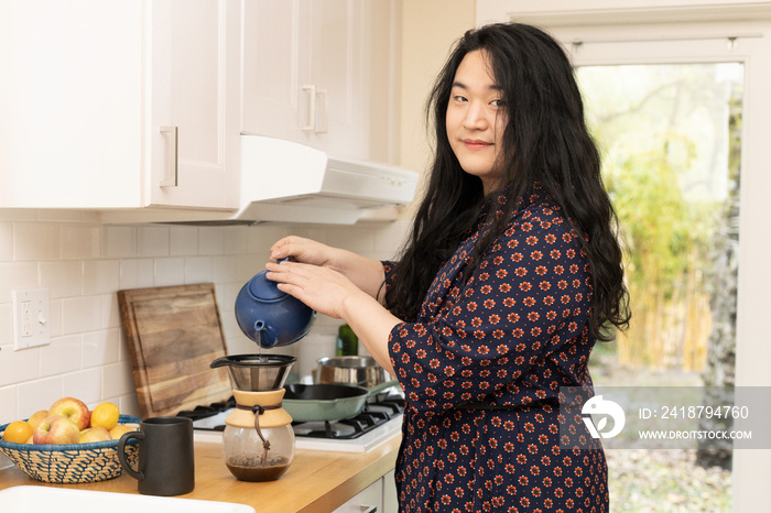 Asian trans woman prepares coffee in the kitchen.