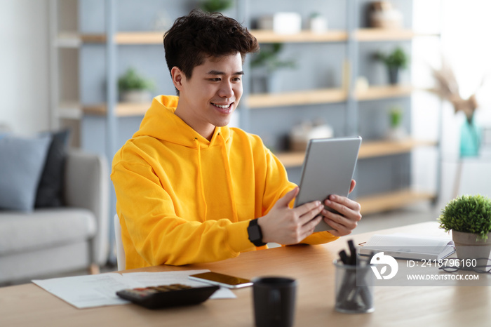 Smiling asian man using digital tablet at home