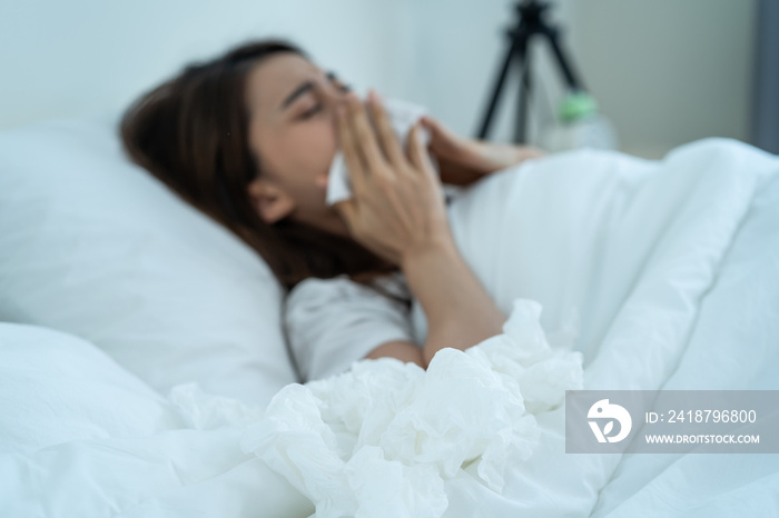 Asian sick girl in pajamas wake up from sleep at night sneezing on bed