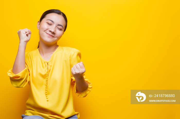 Happy woman make winning gesture isolated over yellow background