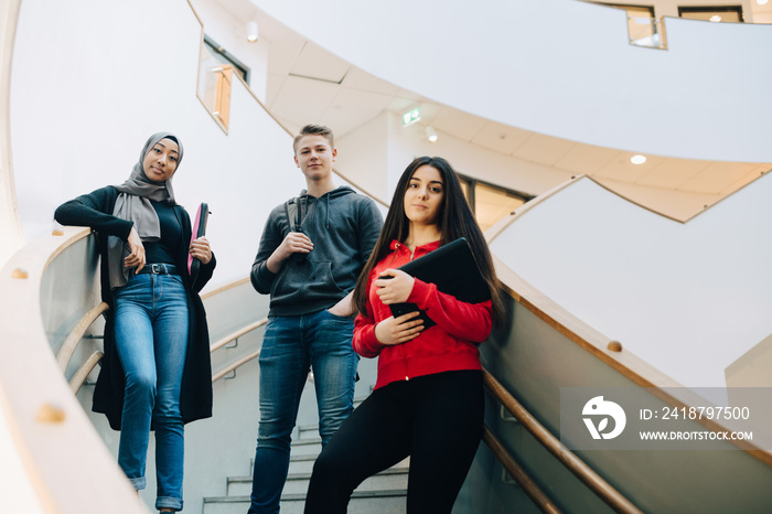 Low angle portrait of students standing on staircase at university