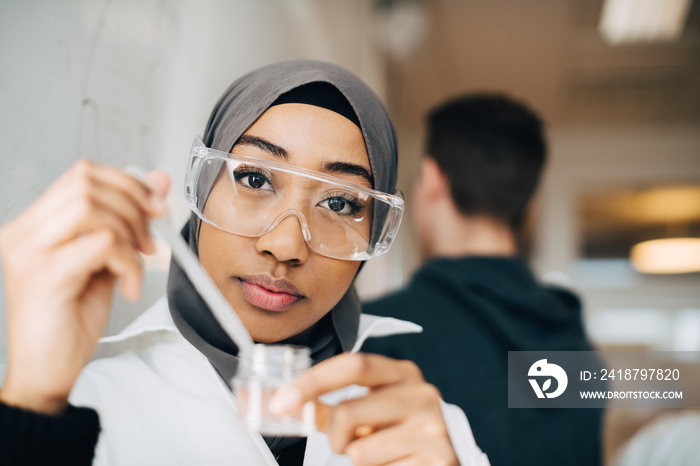 Portrait of teenage student wearing protective eyeglasses doing scientific experiment in chemistry c