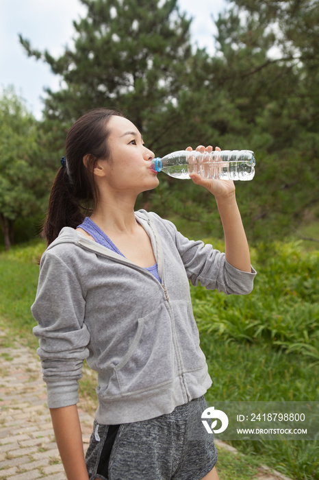 年轻女跑步者在公园喝瓶装水