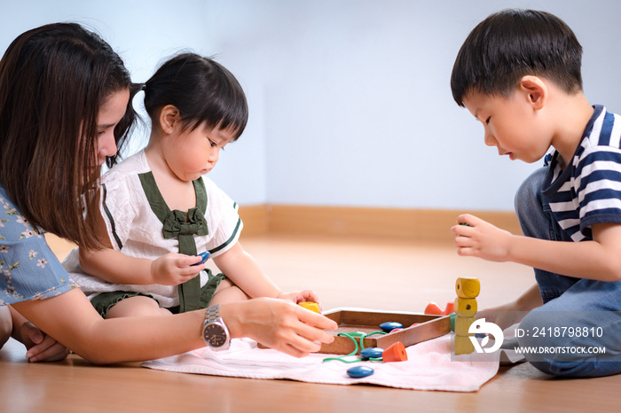 Adorable asian montessori school kids engaged wooden bead thread activity, little girl observing whi