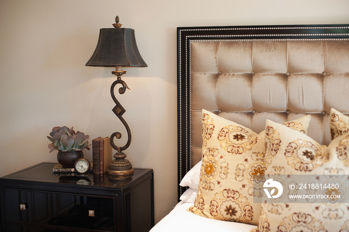 Close-up of throw pillows on bed with lamp on side table in bedroom at home