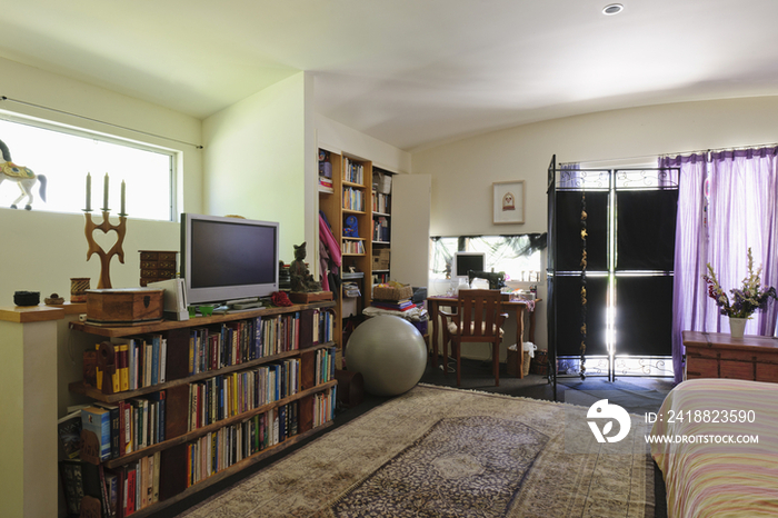 Bookshelves; study table and television with cropped bed in spacious bedroom at house