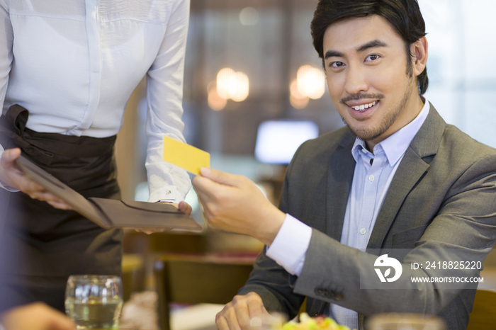 商务男士在餐馆使用信用卡结账