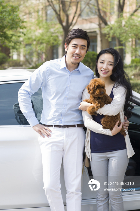 年轻夫妇抱着宠物狗站在车旁