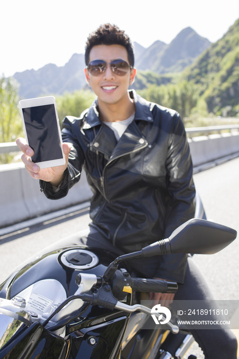 年轻男子骑在摩托车上展示手机