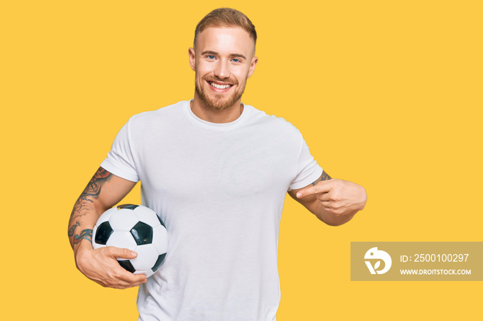 Young irish man holding soccer ball pointing finger to one self smiling happy and proud