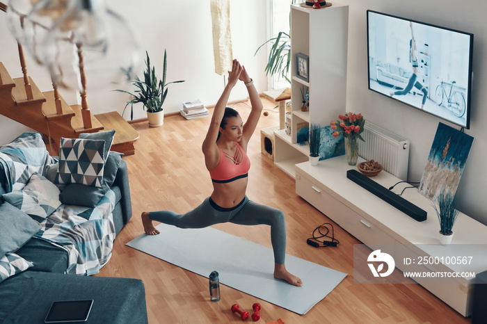 Full length top view of beautiful young woman working out while spending time at home