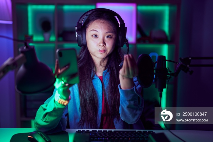 Young asian woman playing video games with smartphone doing italian gesture with hand and fingers confident expression